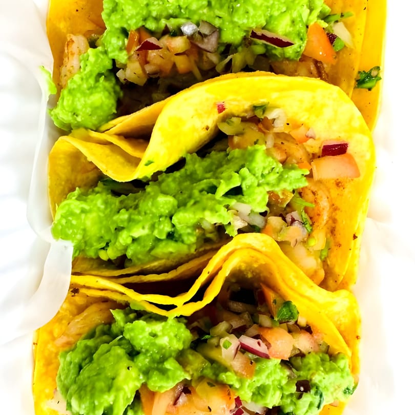 Three vibrant tacos filled with shrimp, pico de gallo, and guacamole, presented in a white holder.